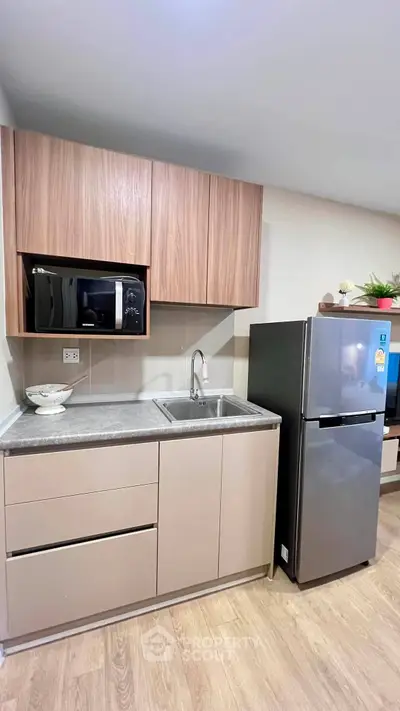 Modern kitchen with sleek cabinetry, stainless steel fridge, and built-in microwave in a cozy apartment.
