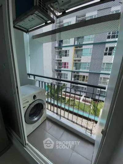 Compact balcony with washing machine overlooking modern apartment complex.