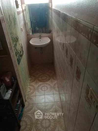 Compact bathroom with tiled walls and floor, featuring a small sink and mirror.