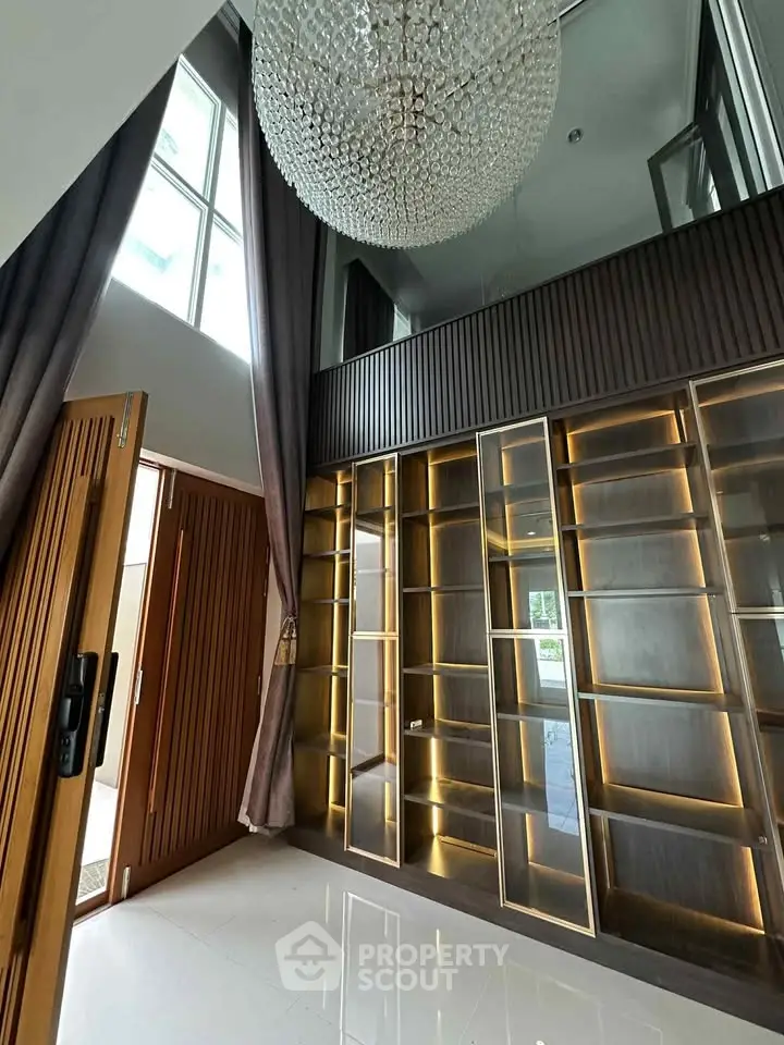Luxurious high-ceiling living room with elegant chandelier and modern glass shelving.
