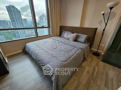 Modern bedroom with city view, featuring a cozy bed and stylish floor lamp.