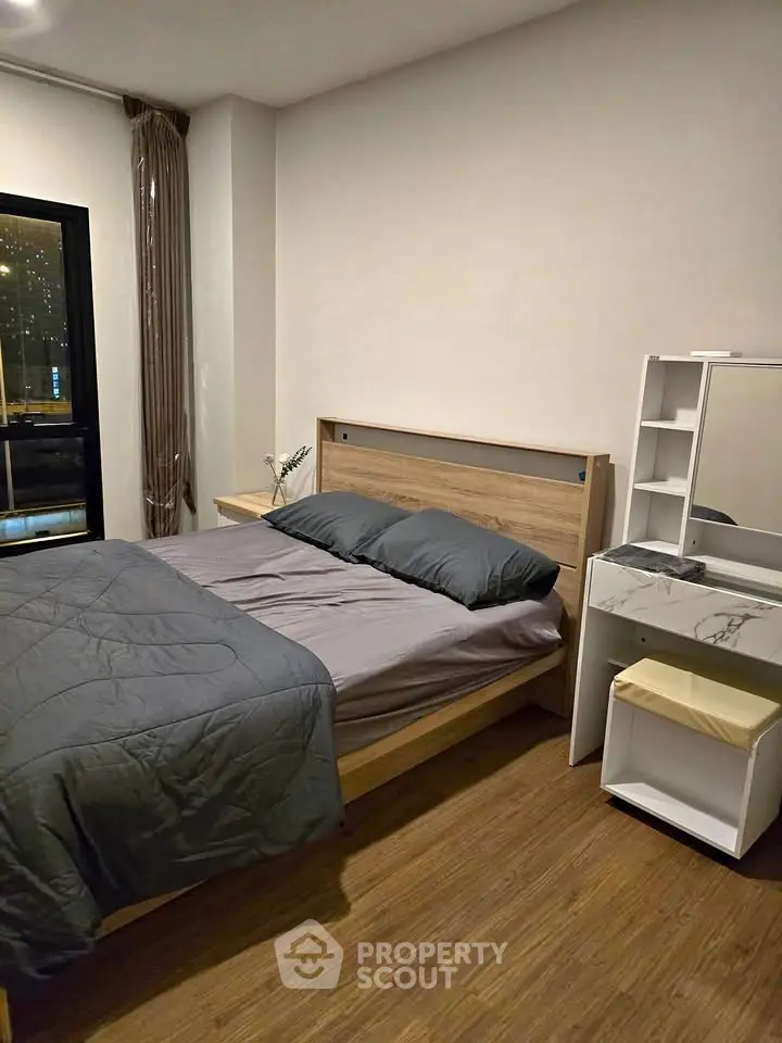 Cozy bedroom with modern wooden furniture and large window offering city view.