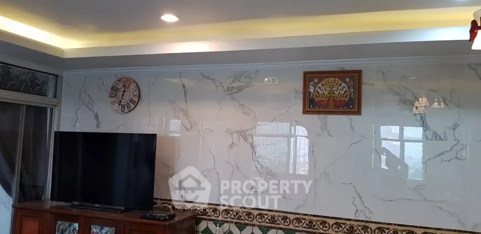 Elegant living room with marble walls and modern lighting, featuring a large TV and stylish decor.