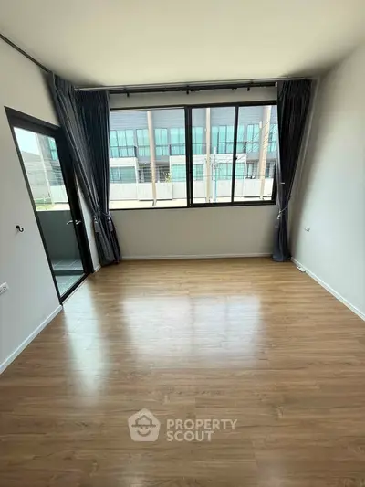 Spacious living room with large windows and balcony access, featuring modern wooden flooring and elegant curtains.