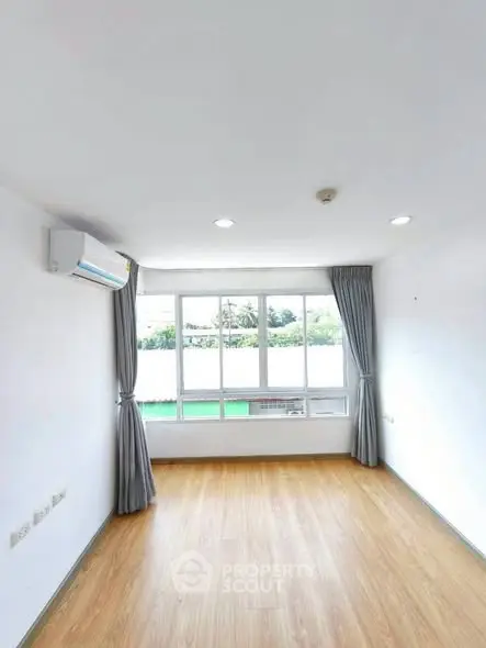 Bright empty room with large window and wooden flooring, ideal for customization.