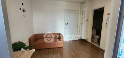 Cozy living room with brown sofa and wooden flooring, adjacent to a bathroom.