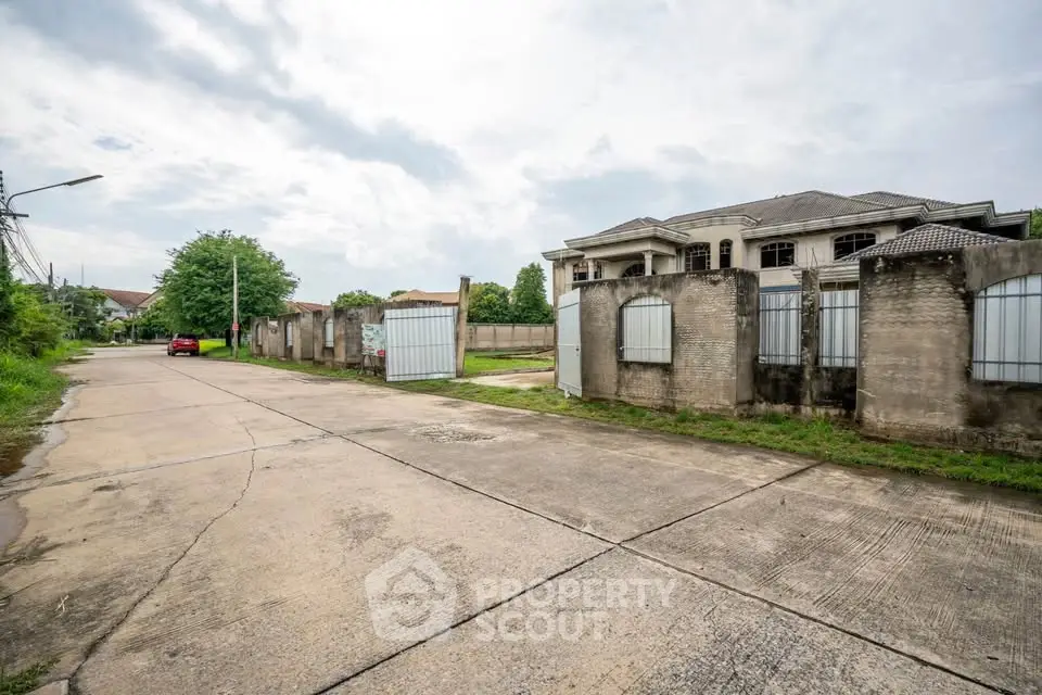 Spacious suburban street view with large gated property and lush greenery.