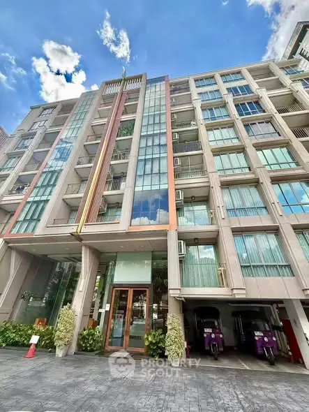 Modern multi-story building with glass facade and parking area under clear blue sky.