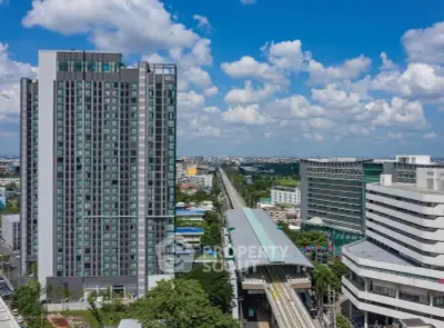 Modern high-rise building with adjacent train station and cityscape view.