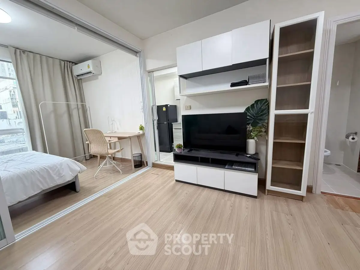 Modern apartment interior with open living room and bedroom, featuring sleek furniture and natural light.