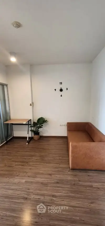 Modern living room with stylish brown sofa and wall clock, featuring sleek wooden flooring and a minimalist desk.