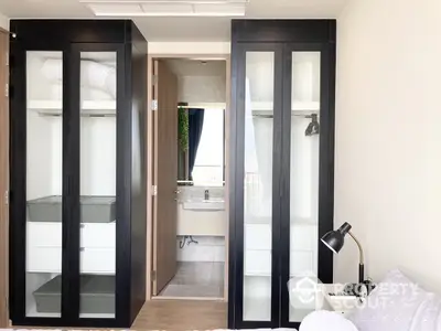 Modern bedroom with sleek black wardrobe leading to an en-suite bathroom, offering a glimpse of a well-lit, tiled bathroom space.