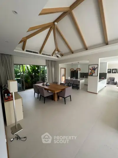 Spacious living room with modern design and wooden ceiling beams, featuring a dining area and open kitchen.