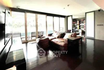 Spacious modern living room with large windows and balcony access, featuring sleek dark flooring and contemporary furniture.