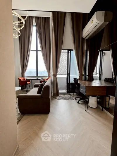 Modern living room with large windows and stylish decor, featuring a cozy seating area and a work desk.