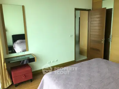 Cozy bedroom with modern decor and wooden flooring, featuring a stylish mirror and comfortable bed.