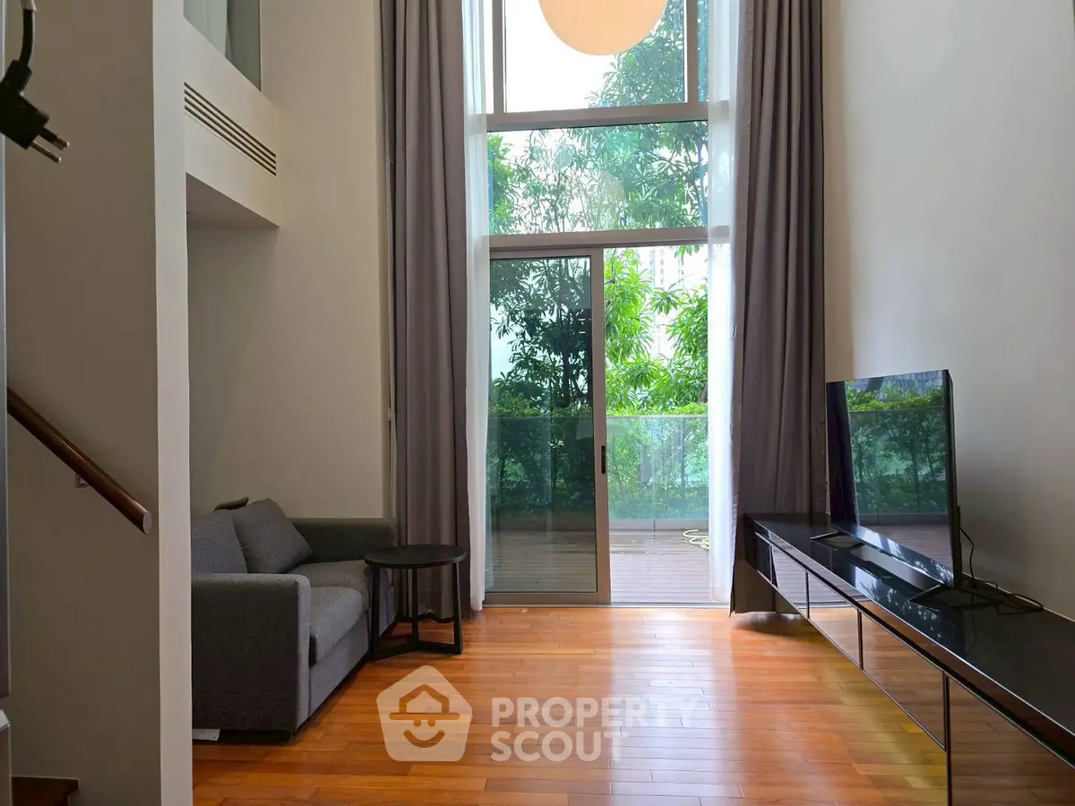 Spacious living room with high ceiling and large windows overlooking lush greenery.