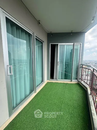 Spacious balcony with artificial grass and city view in modern high-rise apartment.