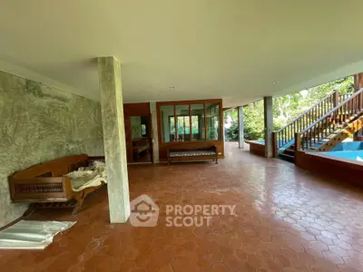Spacious open-plan living area with terracotta flooring and wooden accents, featuring large windows and garden views.