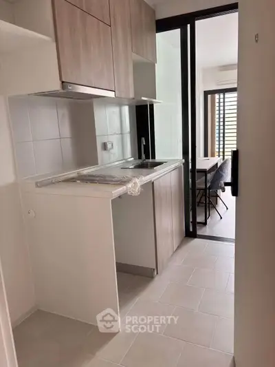 Modern compact kitchen with sleek cabinetry and open layout leading to dining area.