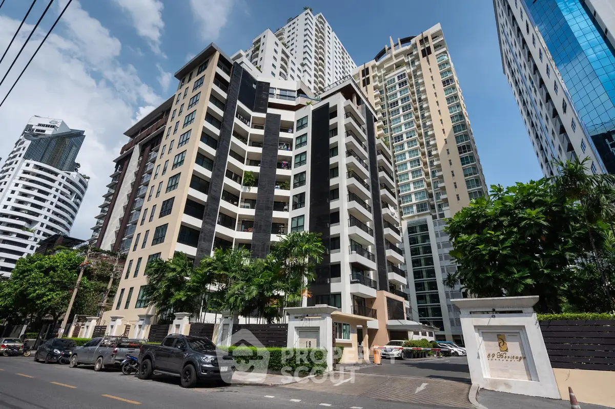 Modern high-rise condominium building with lush greenery and urban skyline view.