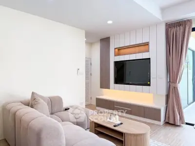 Modern living room with stylish furniture and large TV, featuring natural light and elegant decor.