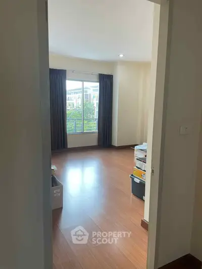 Spacious empty room with wooden flooring and large window view.