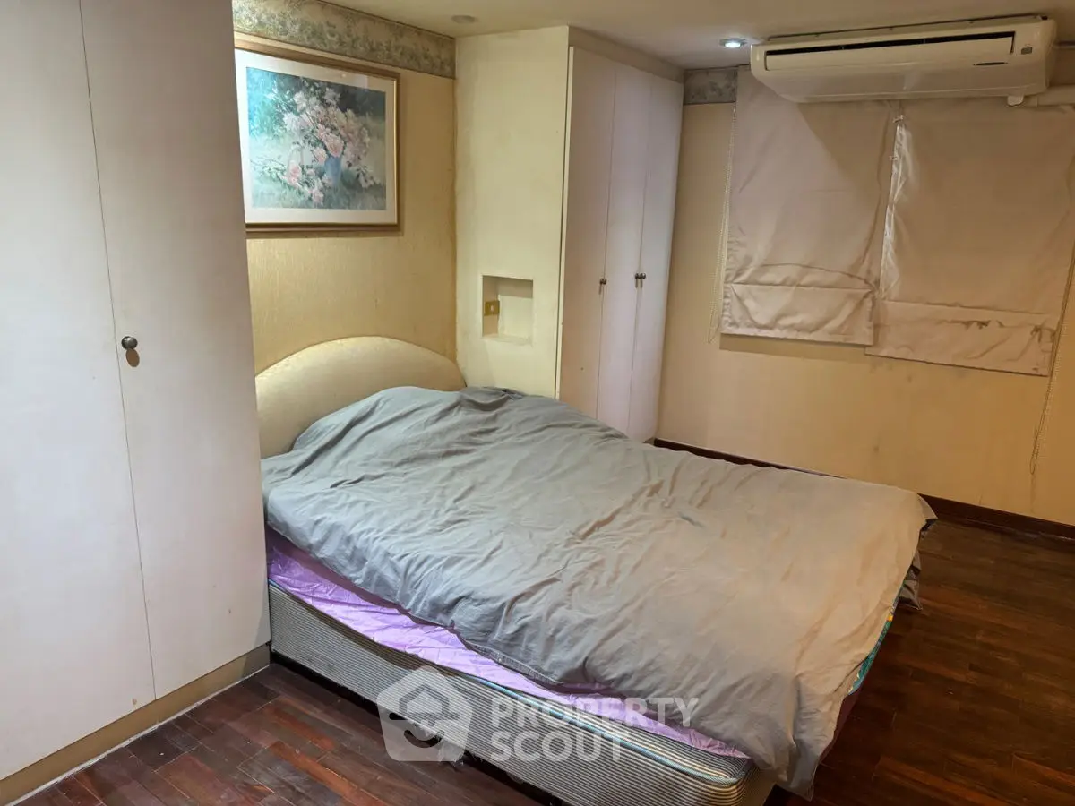 Cozy bedroom with air conditioning and wooden flooring, featuring a comfortable bed and built-in storage.