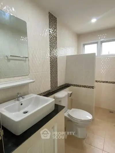 Modern bathroom with sleek sink and toilet, featuring stylish tile accents and natural light.