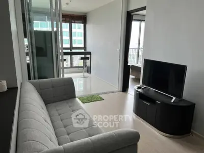 Modern living room with sleek gray sofa and flat-screen TV, featuring a bright balcony view.