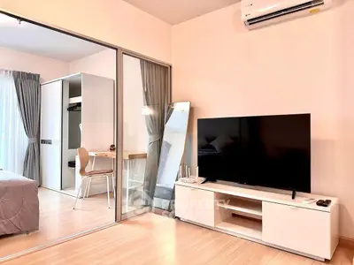 Modern studio apartment with sleek design and large TV, featuring a cozy bedroom and stylish workspace.