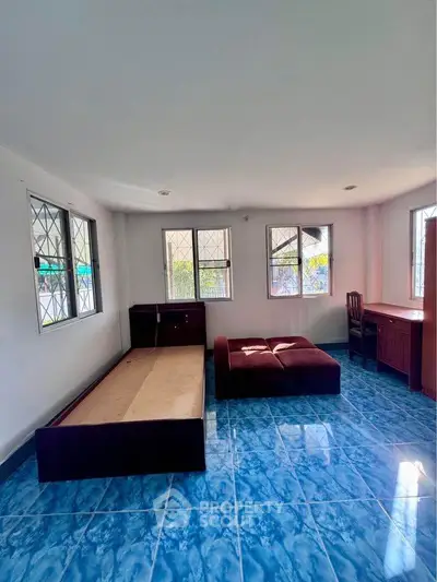 Spacious room with blue tiled floor, featuring a bed frame and desk, ideal for versatile living arrangements.