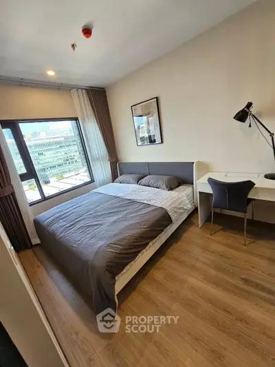 Modern bedroom with city view, stylish desk, and cozy bedding in a high-rise apartment.