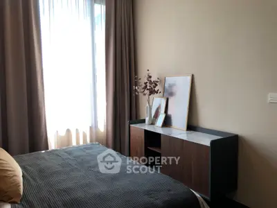 Cozy bedroom with elegant decor and natural light, featuring a stylish cabinet and framed artwork.