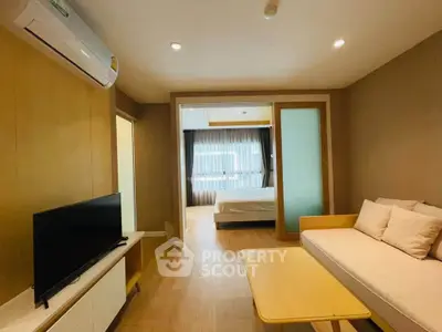 Modern living room with cozy sofa and TV, leading to a bright bedroom with large window.