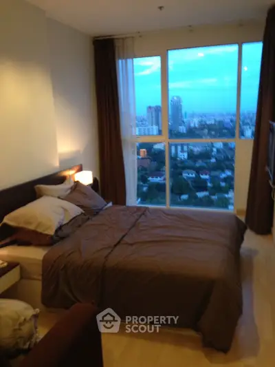 Cozy bedroom with large window offering stunning city view, perfect for relaxation and comfort.