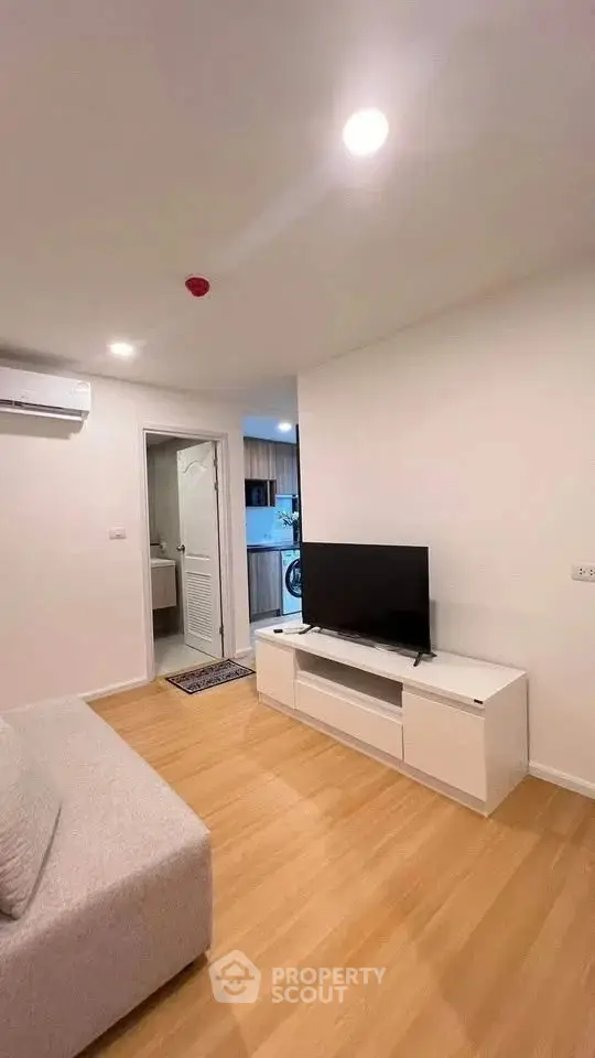 Modern living room with sleek TV stand and cozy sofa, leading to a compact kitchen area.
