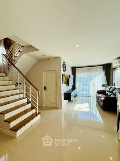 Spacious modern living room with sleek staircase and abundant natural light.