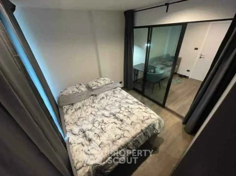 Cozy bedroom with modern decor and sliding glass doors leading to a stylish living area.