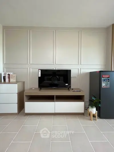 Modern living room with sleek TV stand and refrigerator, showcasing minimalist design and neutral tones.