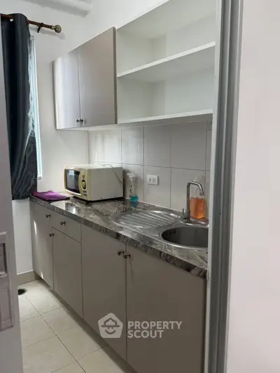 Compact kitchen with modern cabinets and marble countertop, featuring a microwave and sink.