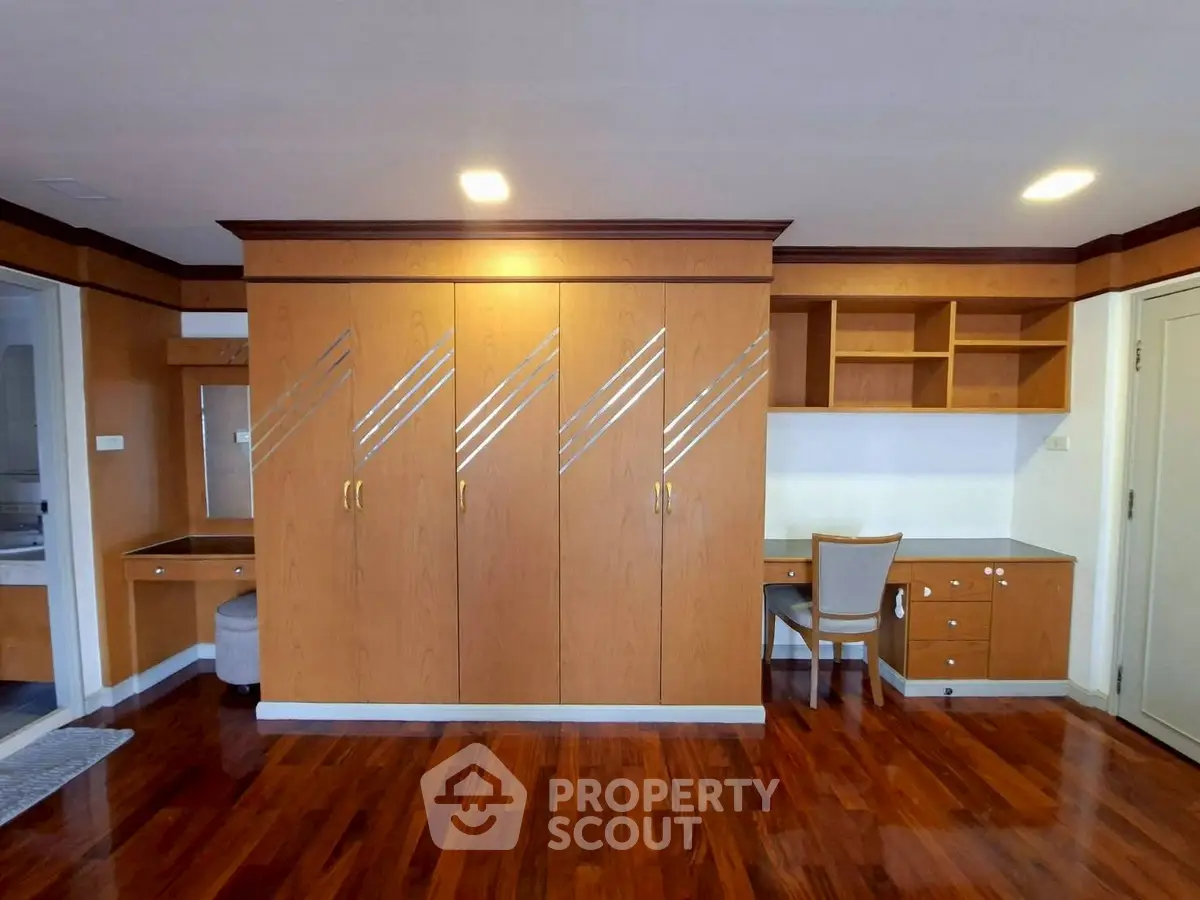 Spacious bedroom with built-in wooden wardrobe and study desk, featuring elegant hardwood flooring.