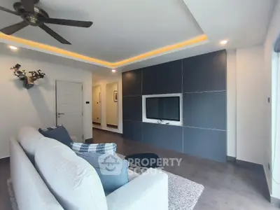 Modern living room with sleek design, featuring a wall-mounted TV, cozy sofa, and stylish ceiling fan.