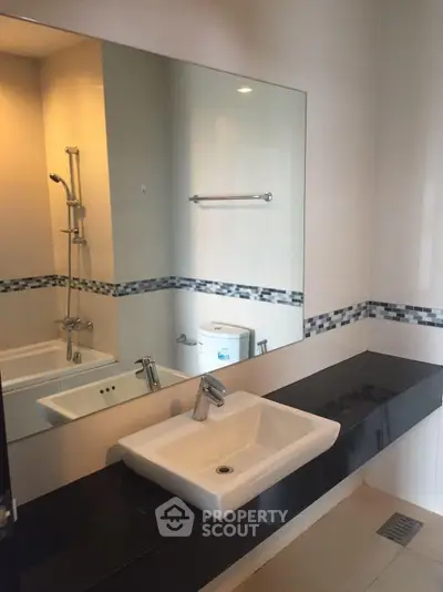 Modern bathroom with sleek sink and large mirror, featuring elegant tile accents and contemporary fixtures.
