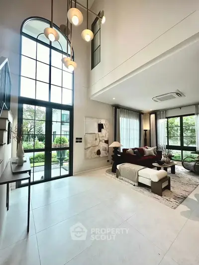 Luxurious living room with high ceilings and elegant decor, featuring large windows and modern lighting.