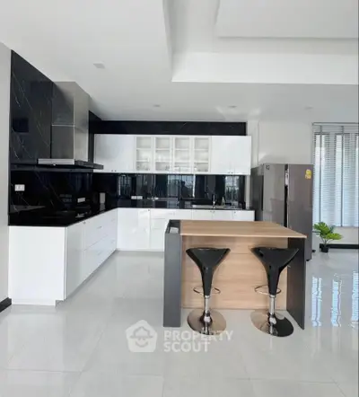 Modern kitchen with sleek black and white design, featuring an island and high stools.
