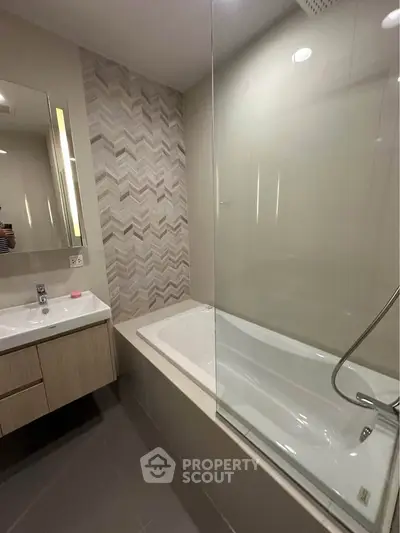 Modern bathroom with stylish tile accent wall and sleek fixtures, featuring a bathtub and vanity.