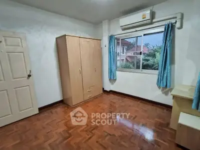 Spacious bedroom with wooden flooring and natural light in modern apartment.