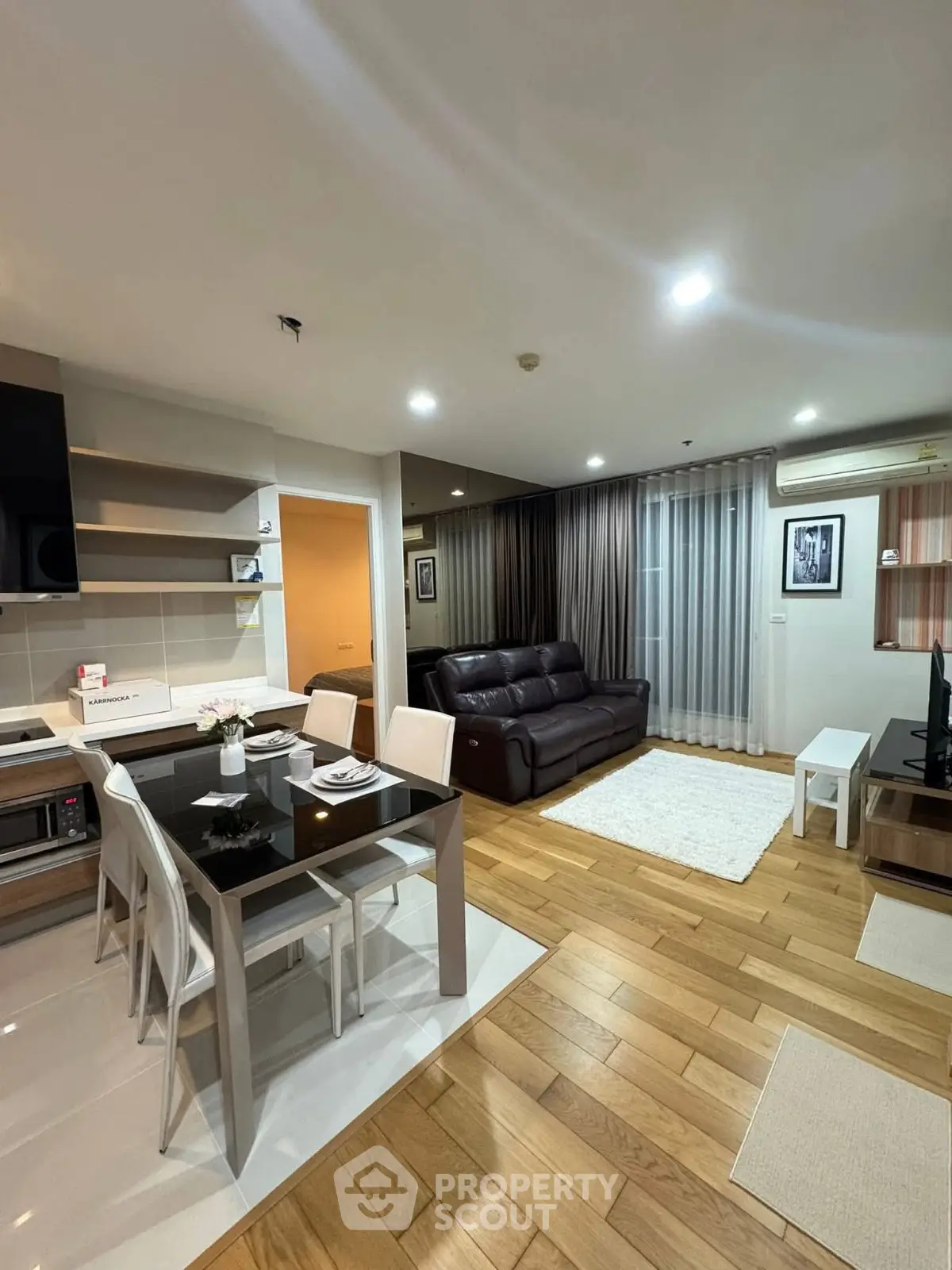 Modern open-layout living room with kitchen, featuring sleek furniture and wooden flooring.