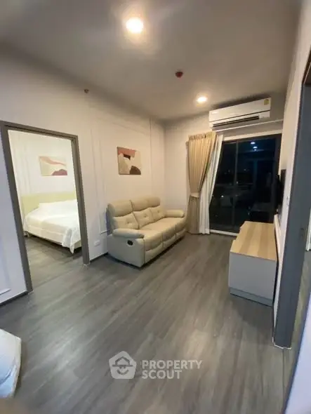 Modern living room with sleek flooring, cozy sofa, and air conditioning, leading to a stylish bedroom.